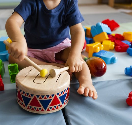A young child playing with a wooden drum on a play mat.