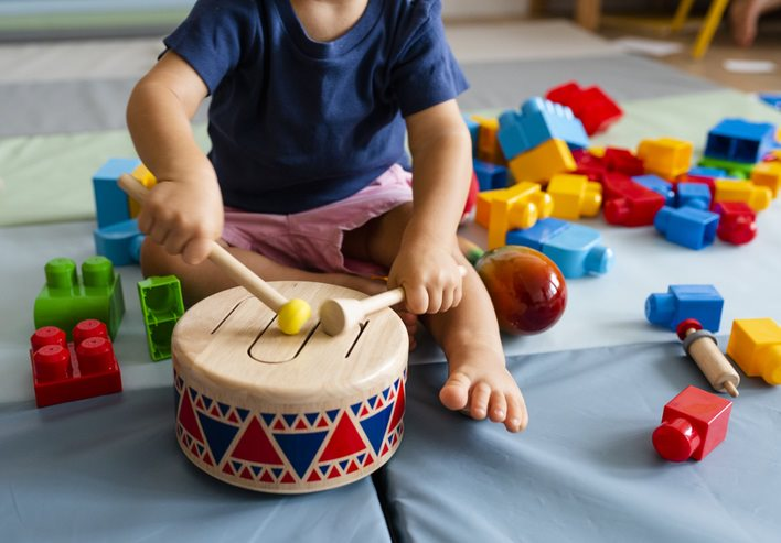 A young child playing with a wooden drum on a play mat.