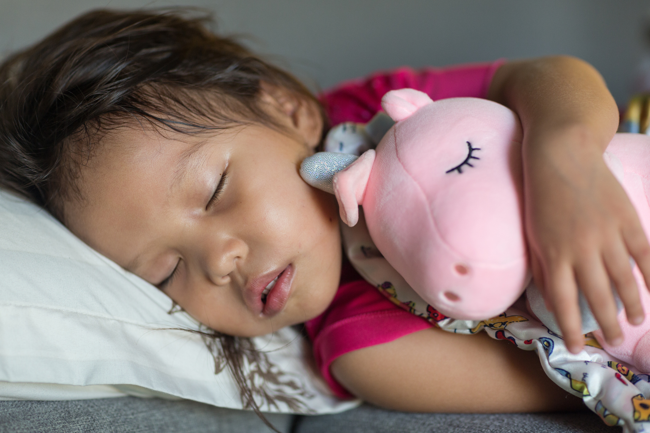 A little girl sleeping with a stuffed pig.