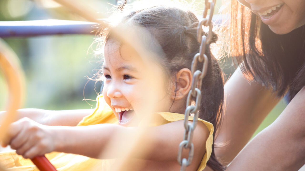 A young girl is playing on a swing with her mother.