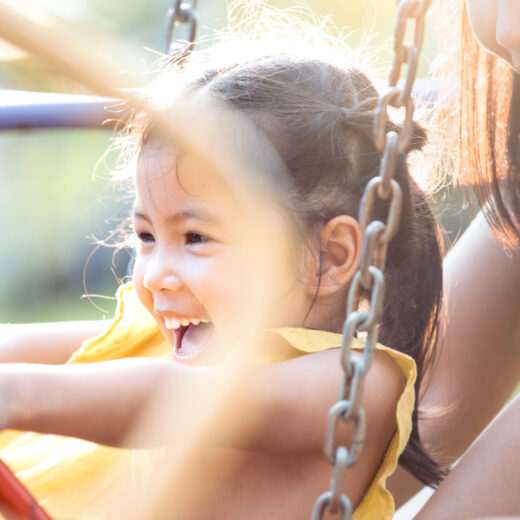 A young girl is playing on a swing with her mother.