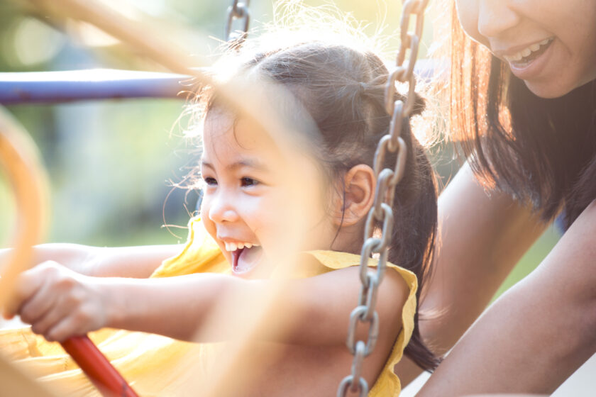 A young girl is playing on a swing with her mother.